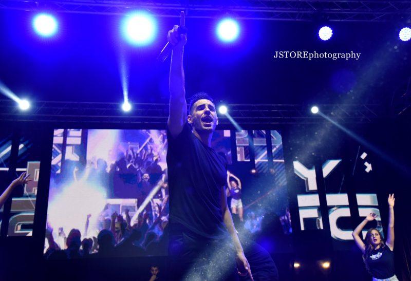 Massimo Manca sul palco con il microfono sotto le luci blu